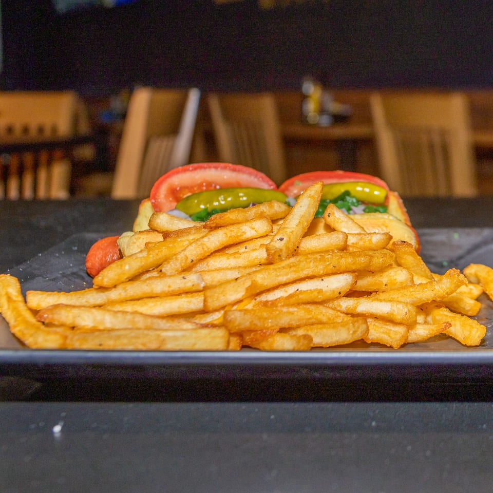 Two hot dogs with tomatoes and relish, served with a large pile of golden french fries.