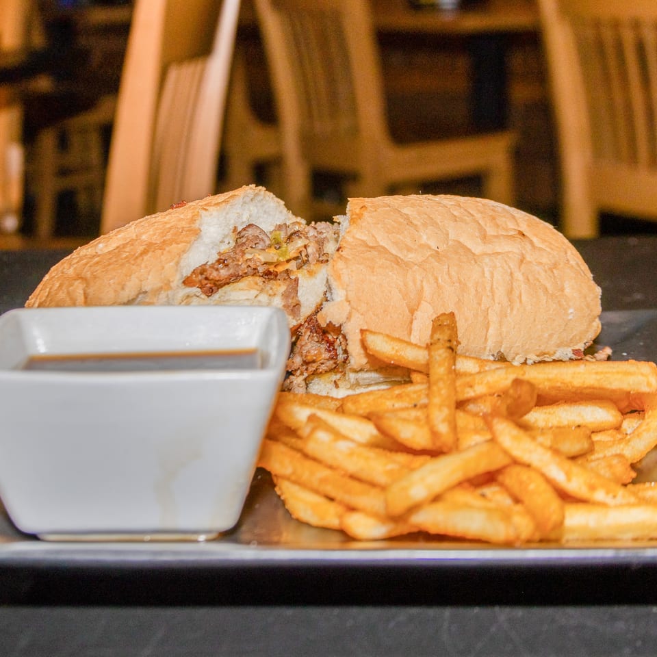 A Cobalt Bar & Grill cheesesteak sandwich, cut in half, with fries and a side of au jus.