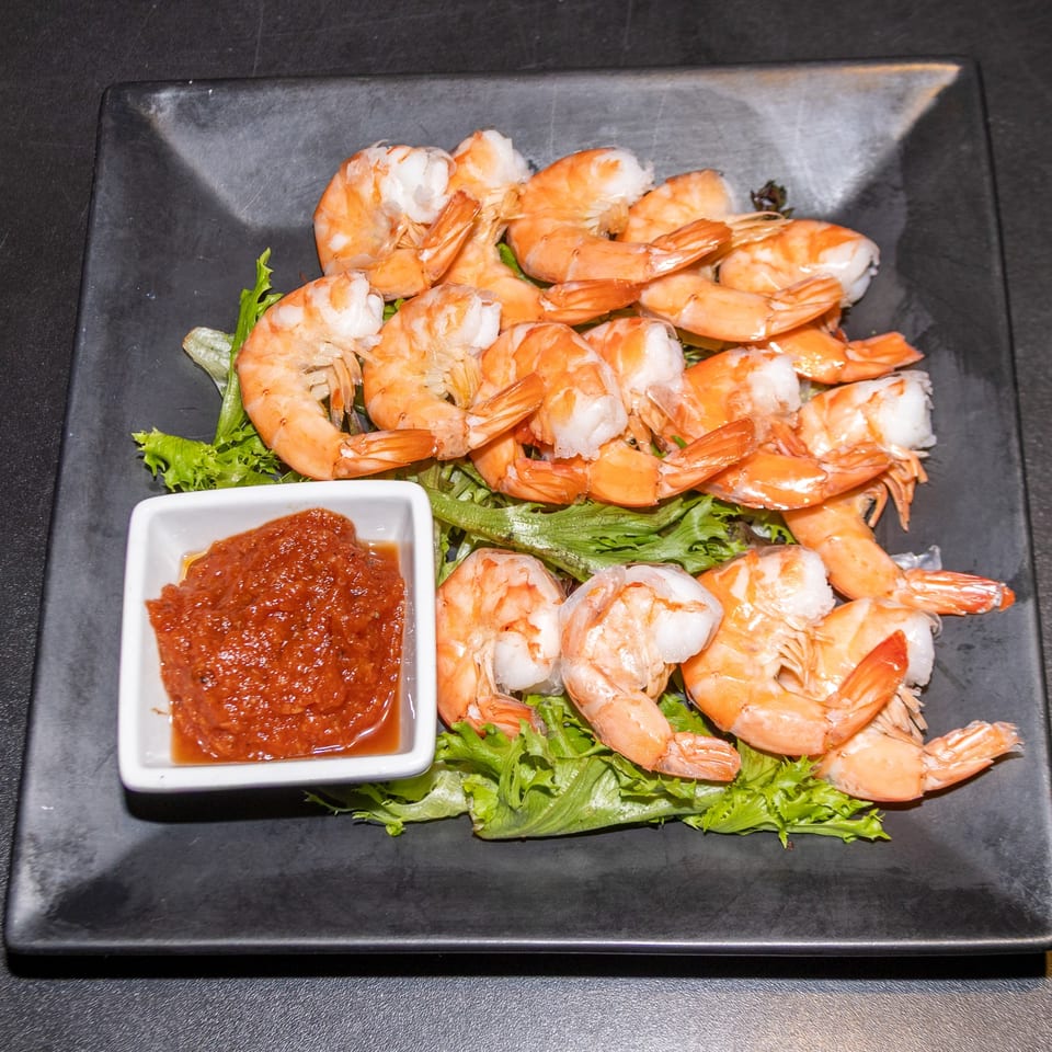 A plate of shrimp cocktail with red sauce on a bed of lettuce at Cobalt Bar & Grill.
