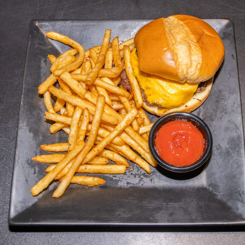 Cheeseburger with melted cheese, a pile of golden fries, and a side of ketchup on a dark plate.